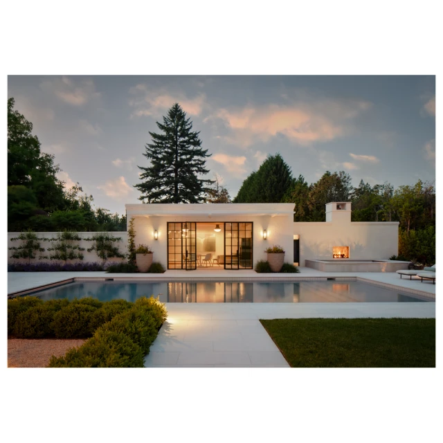 Exterior view of a modern house with a pool and an outdoor fireplace, surrounded by trees under a twilight sky with scattered clouds.