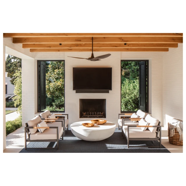 Outdoor living space featuring cushioned chairs surrounding a concrete table, with an outdoor fireplace and ceiling fan.