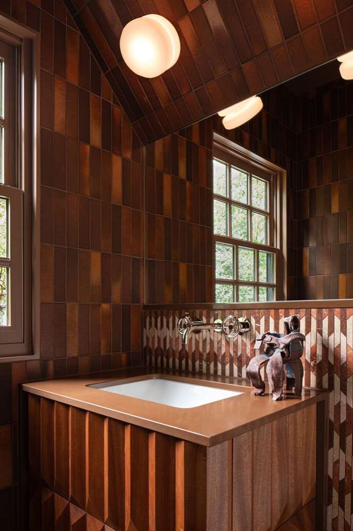 Bathroom interior with a sink, faucet, decorative figurines, a window with a view, and tiled walls and ceiling in brown tones.