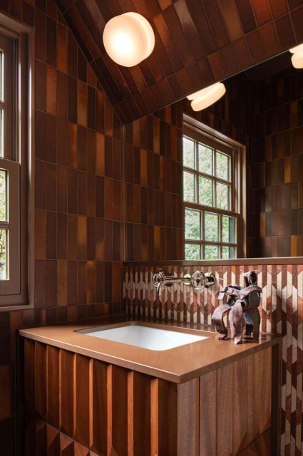 Bathroom interior with a sink, faucet, decorative figurines, a window with a view, and tiled walls and ceiling in brown tones.