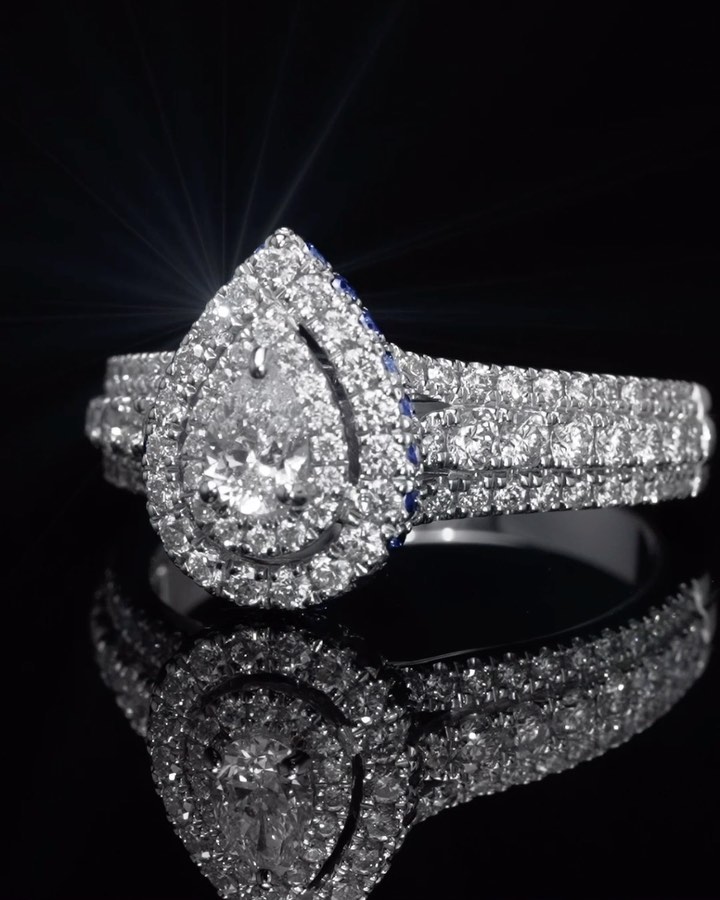 Sparkling pear-shaped diamond ring with a halo setting, set against a dark reflective surface, emphasizing its brilliance and design.