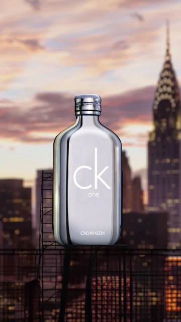 Calvin Klein CK One fragrance bottle stands prominently with city skyline background at dusk, product photography, beauty and fashion.