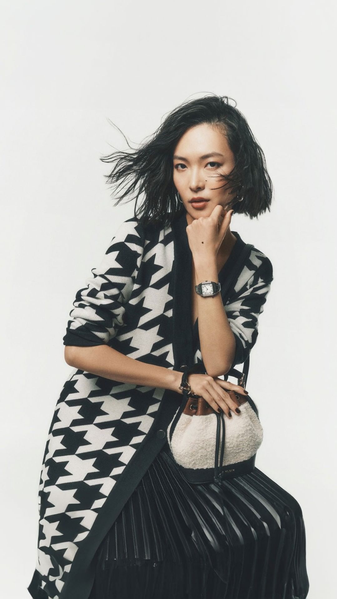Asian woman with dark short hair wearing a black and white houndstooth cardigan against a plain white background