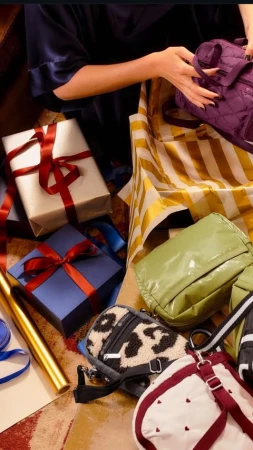 A person is packing a variety of handbags and gift-wrapped boxes with ribbons into a yellow and white striped box, creating a vibrant scene.