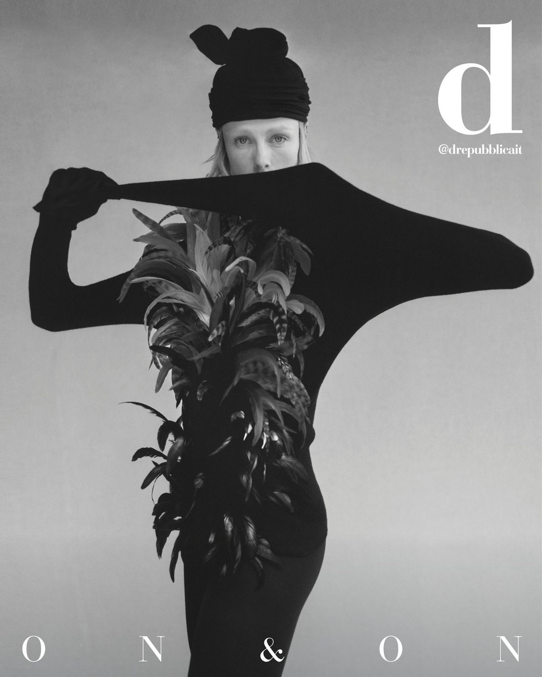 Monochrome fashion shot features a model in a black outfit and feathered garment against a neutral backdrop, highlighting editorial style.