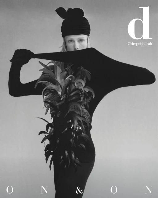 Monochrome fashion shot features a model in a black outfit and feathered garment against a neutral backdrop, highlighting editorial style.