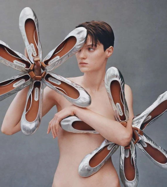 Fashion shot featuring a woman with short hair posing with silver ballet flats, artistic composition against a neutral grey backdrop.