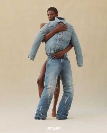 An adult African-American man with bare torso embraces denim jacket and jeans against neutral backdrop in a fashion editorial for Jacquemus.