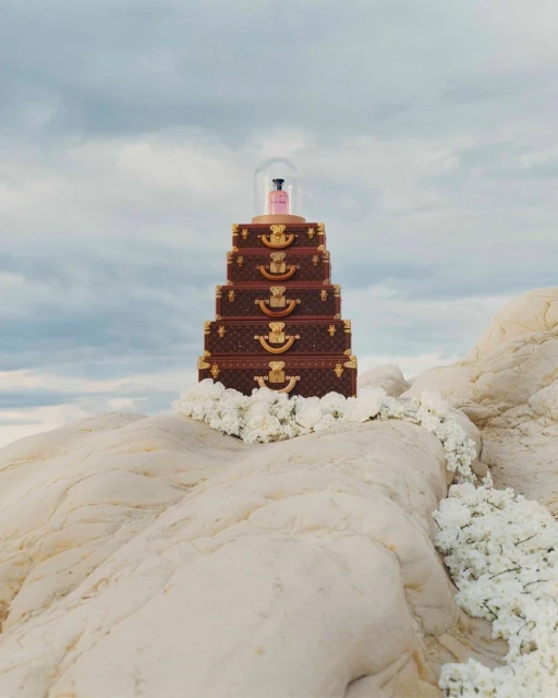 Louis Vuitton stacked luggage on a rock formation, decorated with white flowers, against a cloudy sky, luxury travel and style.