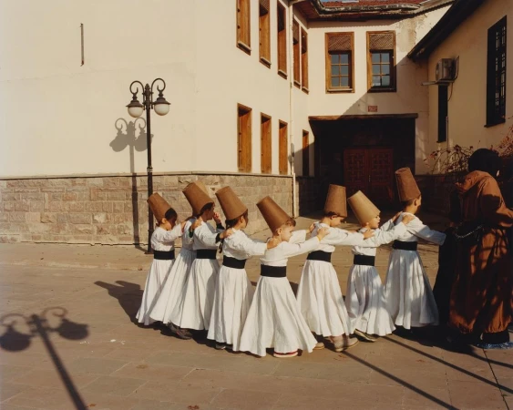 Children in traditional attire participate in a whirling dervish ceremony outdoors on a paved surface, with a building in the background.