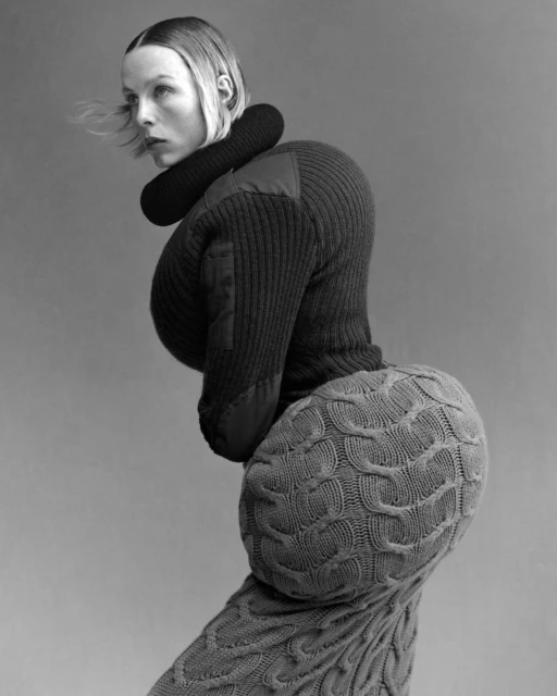 Monochrome studio shot of a fair-skinned adult woman wearing oversized knitwear with rounded shapes around the body.