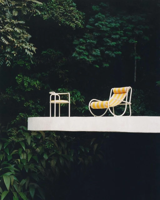 Outdoor furniture on a white patio with a chair and lounger, set against lush green foliage for a minimalist outdoor living space.