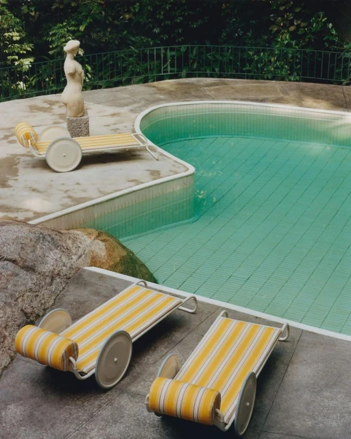 Outdoor shot showcasing poolside lounge chairs with yellow stripes near a pool and statue in a backyard setting.