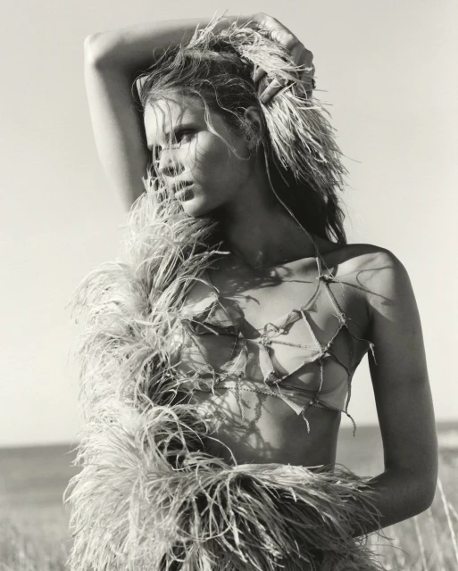 Black and white portrait of a woman outdoors with a feathery garment, eyes glancing left, posing in natural light against a neutral sky.