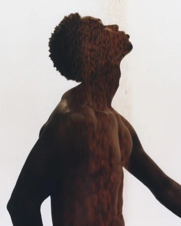 An artistic portrait of an African American male in a shower, looking upward with an expressive pose and dappled light on the body.