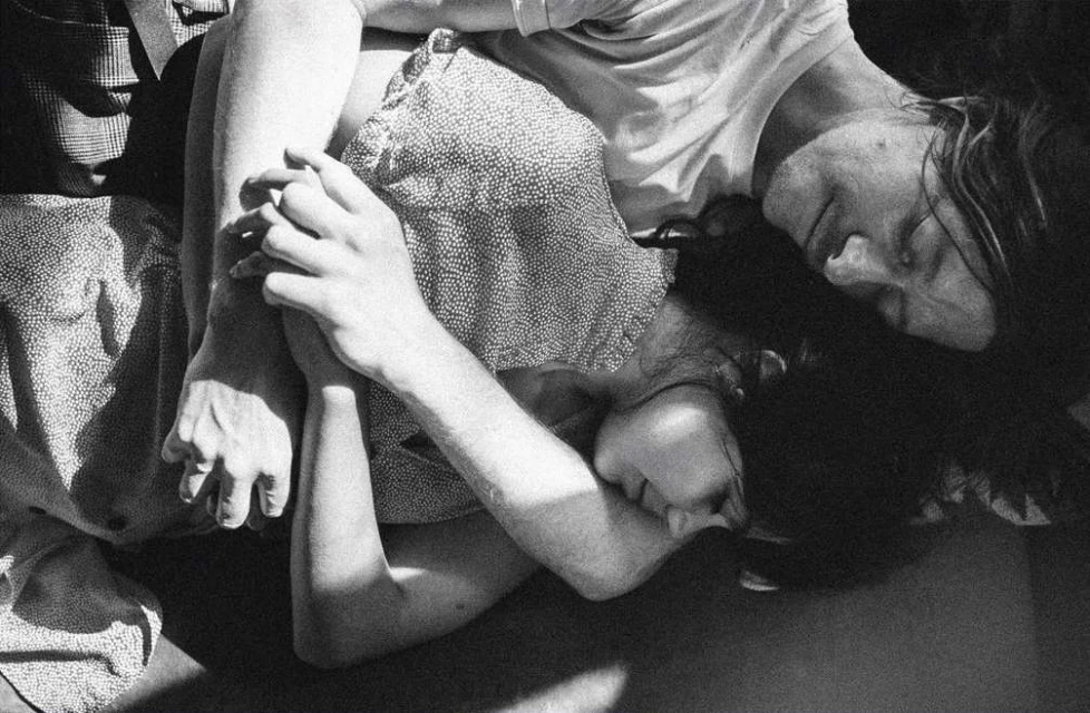 Monochrome portrait of two adults embracing, with a woman in a patterned dress and a person in a white t-shirt; black and white style.