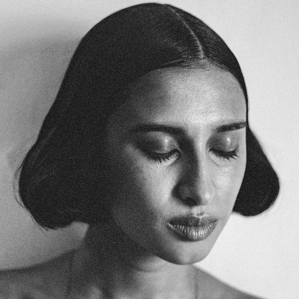 Close-up monochrome portrait of a woman with her eyes closed and dark hair styled in a center part, captured by Theo Gosselin.