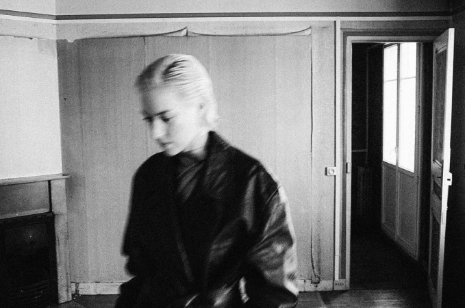 Black and white portrait of a blond woman in a dark leather jacket inside an interior room captured with motion blur.