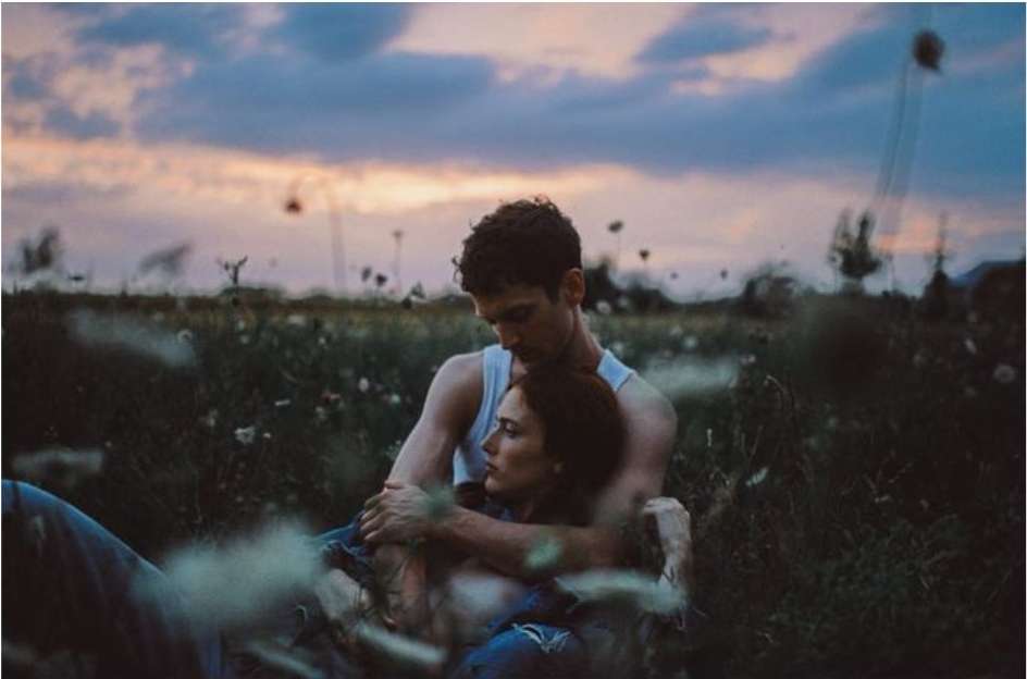 Romantic outdoor portrait of a young couple embracing in a grassy field at dusk, showcasing their connection and the tranquil setting.