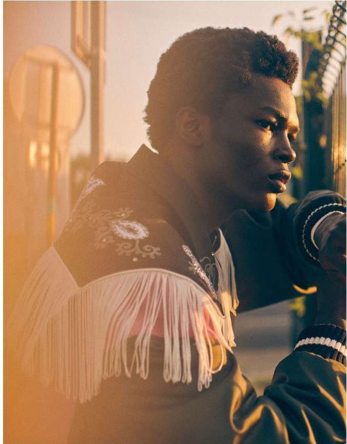 Portrait of a handsome African American man in a brown jacket with white fringe standing outdoors at golden hour.