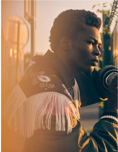 Portrait of a handsome African American man in a brown jacket with white fringe standing outdoors at golden hour.
