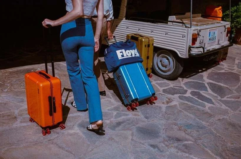 Passengers with rolling luggage near vintage service vehicle, ready for travel. Travel bags in shades of blue, orange, and gold.