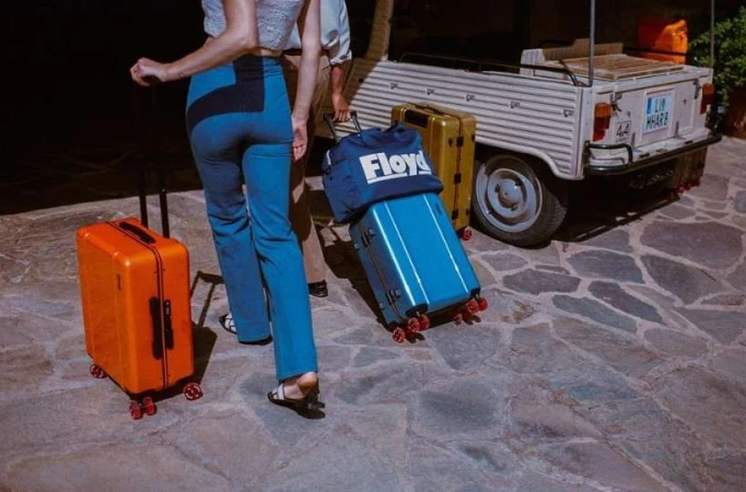 Passengers with rolling luggage near vintage service vehicle, ready for travel. Travel bags in shades of blue, orange, and gold.