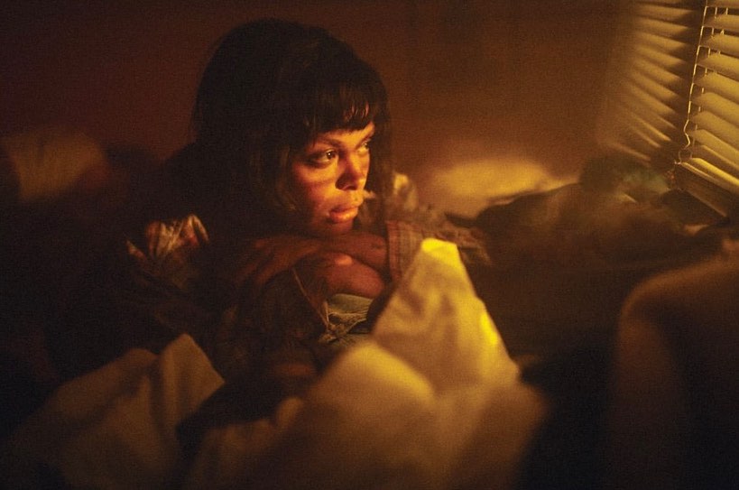 Indoor portrait of an adult woman with dark hair in a dimly lit room with light coming through window blinds.