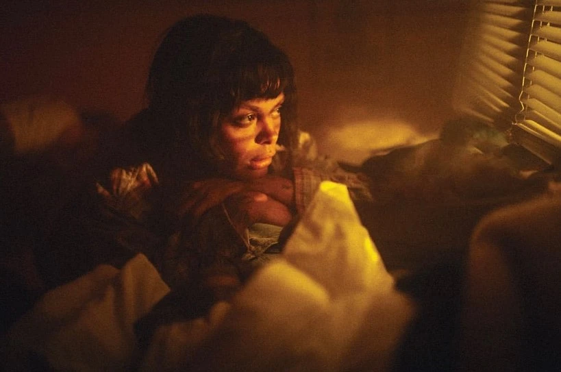 Indoor portrait of an adult woman with dark hair in a dimly lit room with light coming through window blinds.