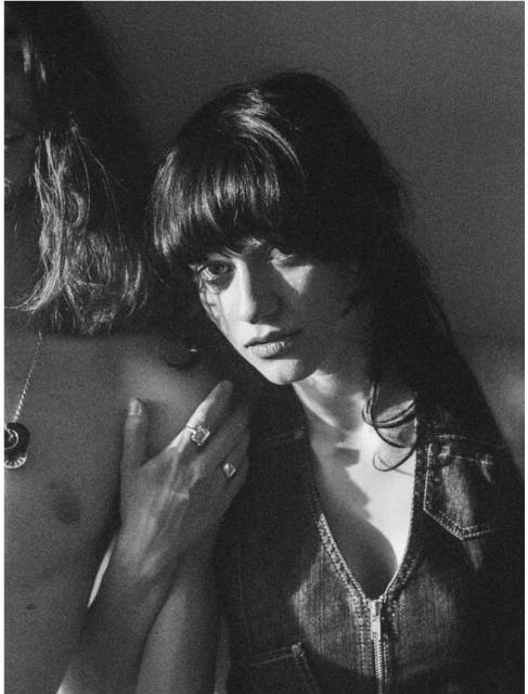 Black and white portrait of a woman with bangs and a denim top, standing next to a partially visible person with long hair.