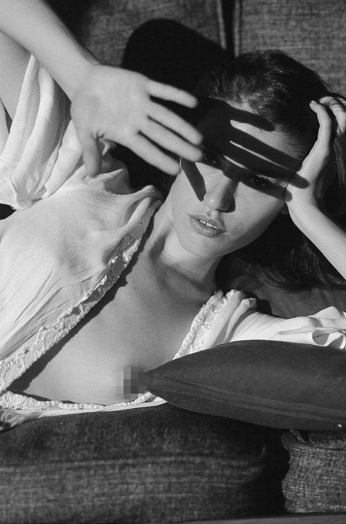 Black and white studio shot of a woman lying down covering her face with her hand with a fabric top and a dark cushion.