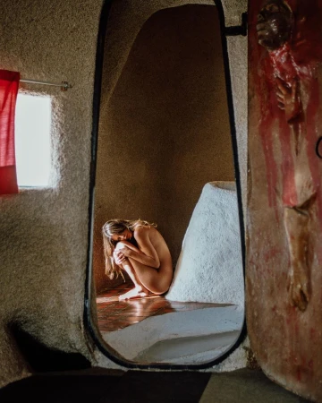 A woman crouches nude inside an arched, textured concrete alcove photographed by Theo Gosselin.