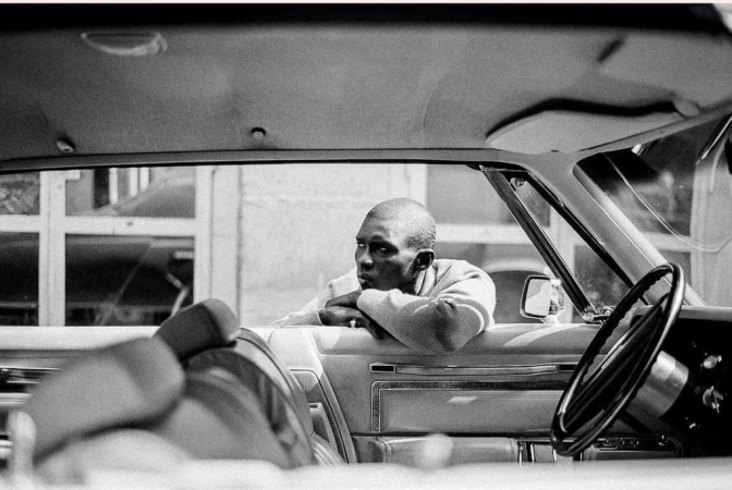 Black and white portrait of a man resting arms on a car window, photographed by Theo Gosselin.