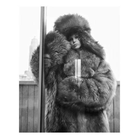 Model in large fluffy fur coat and matching ushanka hat posing indoors by window with city view, photographed by Theo Sion.