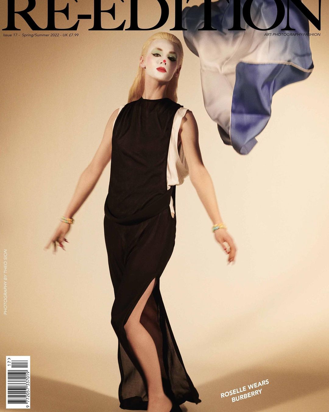 Fashion magazine cover featuring a person in a long black dress with an asymmetrical hemline, striking makeup, and a blonde wig. 