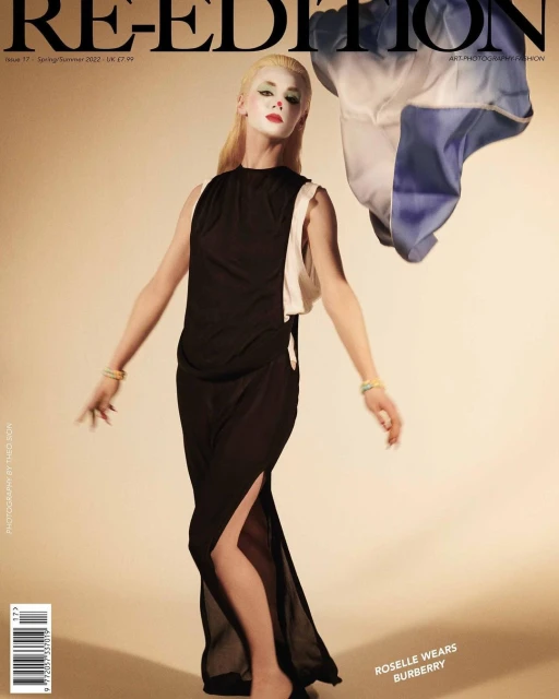 Fashion magazine cover featuring a person in a long black dress with an asymmetrical hemline, striking makeup, and a blonde wig. 