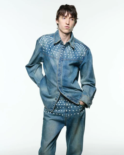 Man in light blue denim shirt and matching jeans with white polka dots, posing in a bright photo studio, fashion editorial.