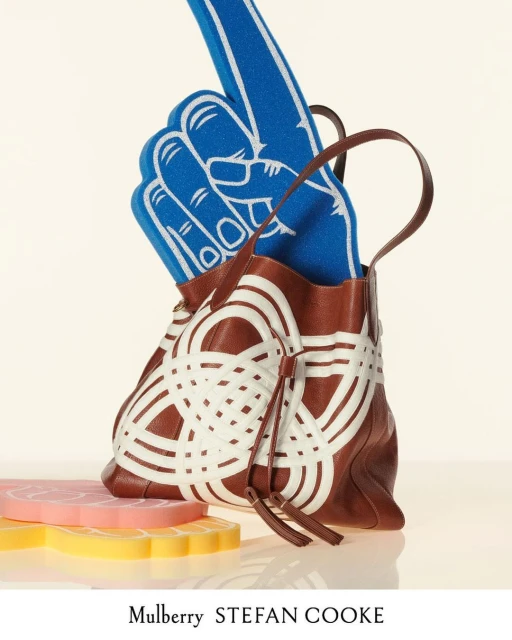 Brown leather handbag with white graphic design and blue foam finger prop. Fashion product shot on white background, luxury accessory.
