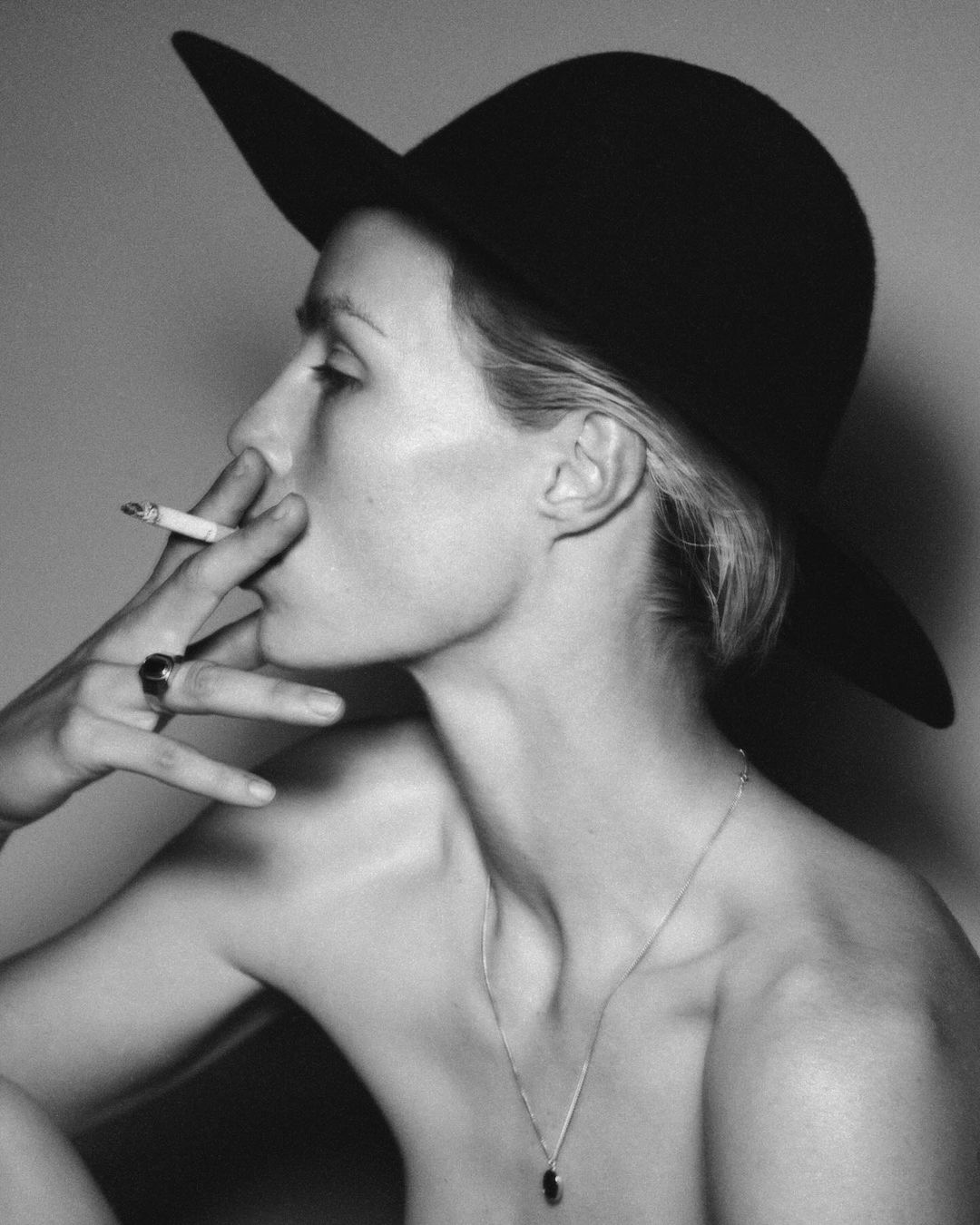 Monochrome portrait of a woman in profile wearing a wide-brimmed black hat, smoking a cigarette