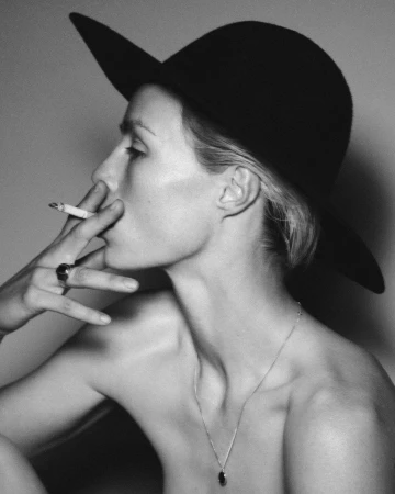 Monochrome portrait of a woman in profile wearing a wide-brimmed black hat, smoking a cigarette