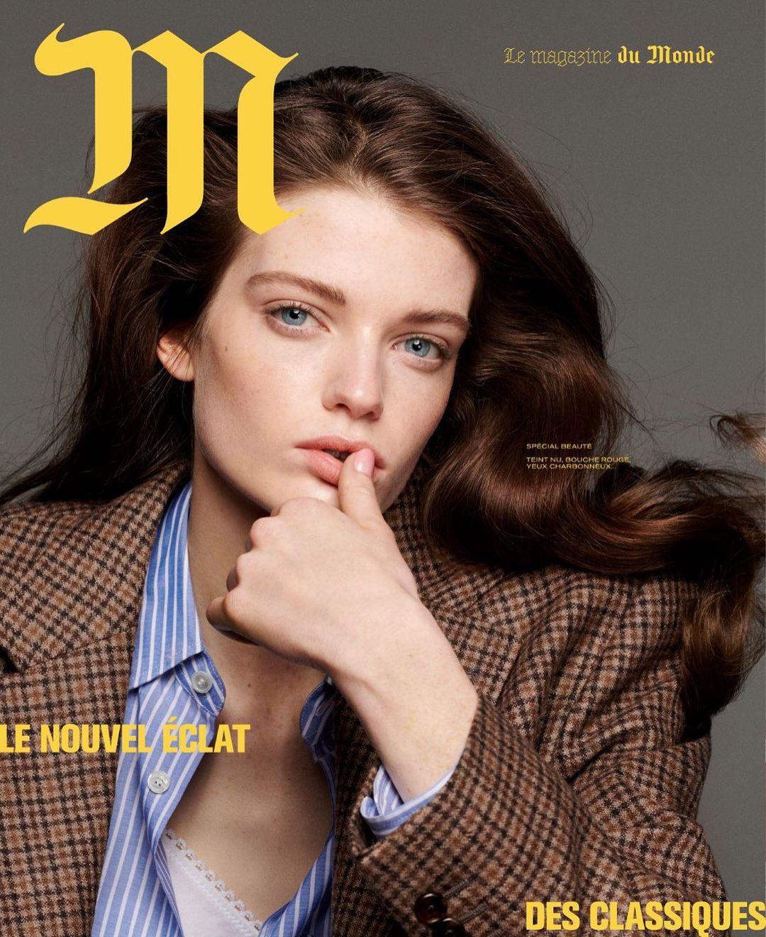 Magazine cover featuring a young adult woman with brown hair and blue eyes, wearing a blazer and striped shirt, against a grey background.