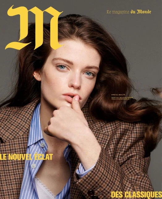 Magazine cover featuring a young adult woman with brown hair and blue eyes, wearing a blazer and striped shirt, against a grey background.