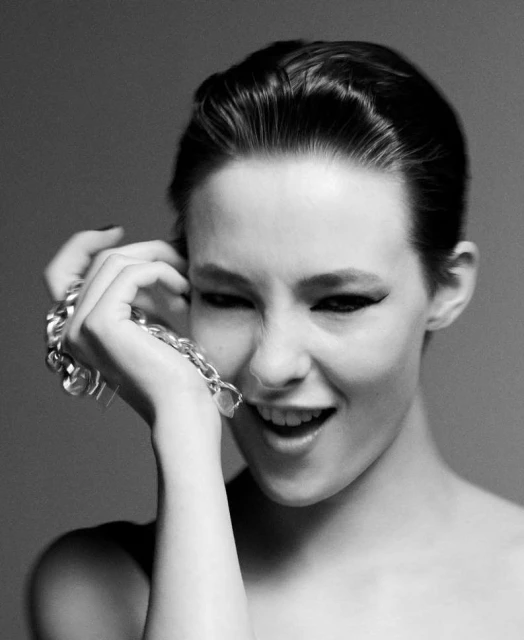 Close-up black and white portrait of a young woman with short dark hair, bold eyeliner, and a silver chain around her hand.