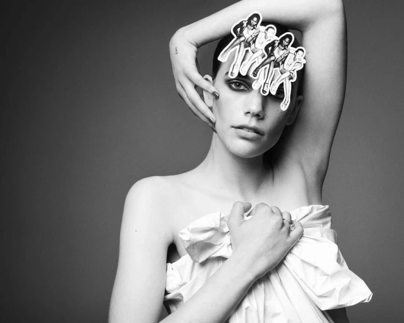 Striking black and white portrait of a woman with hand on head, styled with retro figures, against a grey backdrop in studio lighting.