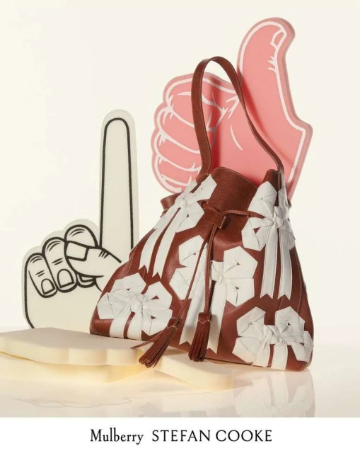 Brown leather bucket bag with white decorative accents, styled with white foam fingers on a white surface and background.