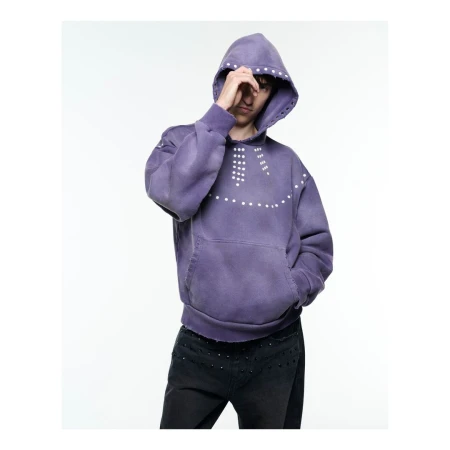 Person wearing a purple hoodie with white studs posing in a photo studio with white seamless backdrop looking towards camera.