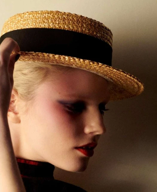 Close-up portrait of a fair-skinned adult female wearing a straw boater hat with a black band, dark eye makeup, and red lipstick.