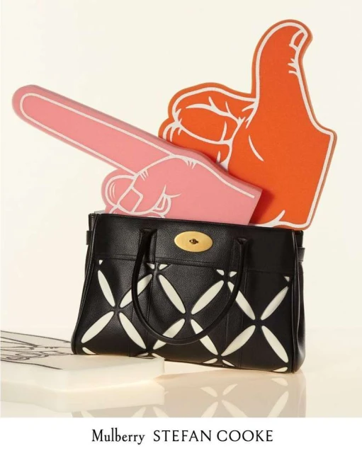 Studio shot of a black Mulberry purse with white design and foam fingers in pink and orange against a light beige background.
