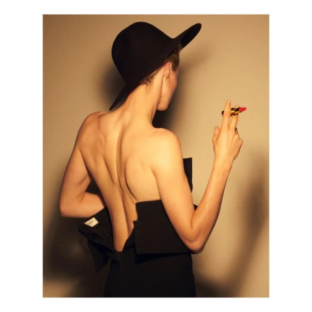 Model from behind wearing a black wide-brim hat and black dress holding a red lipstick, photographed by Theo Sion.