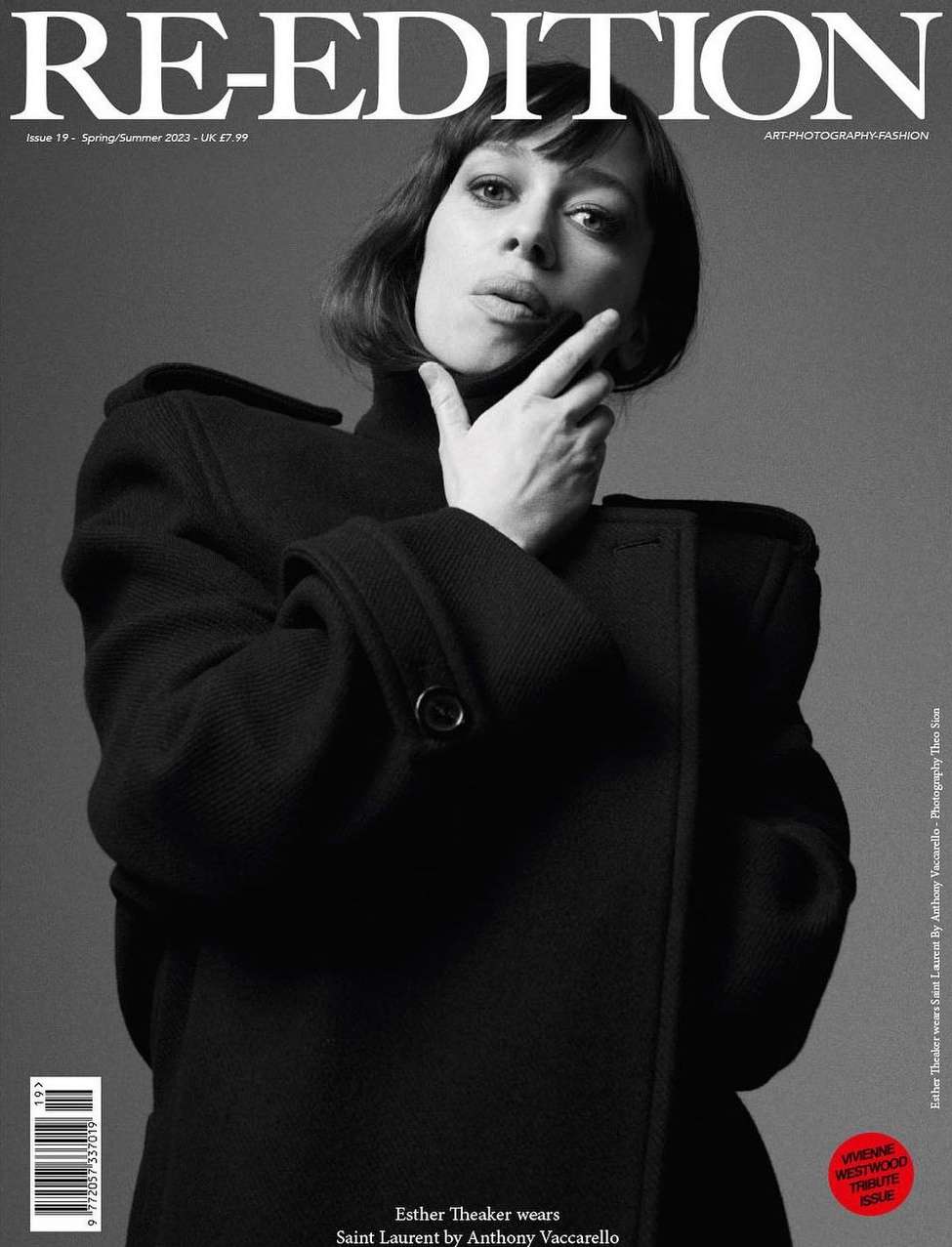 Portrait of a woman wearing a heavy black structured coat against a plain grey backdrop for a magazine cover.